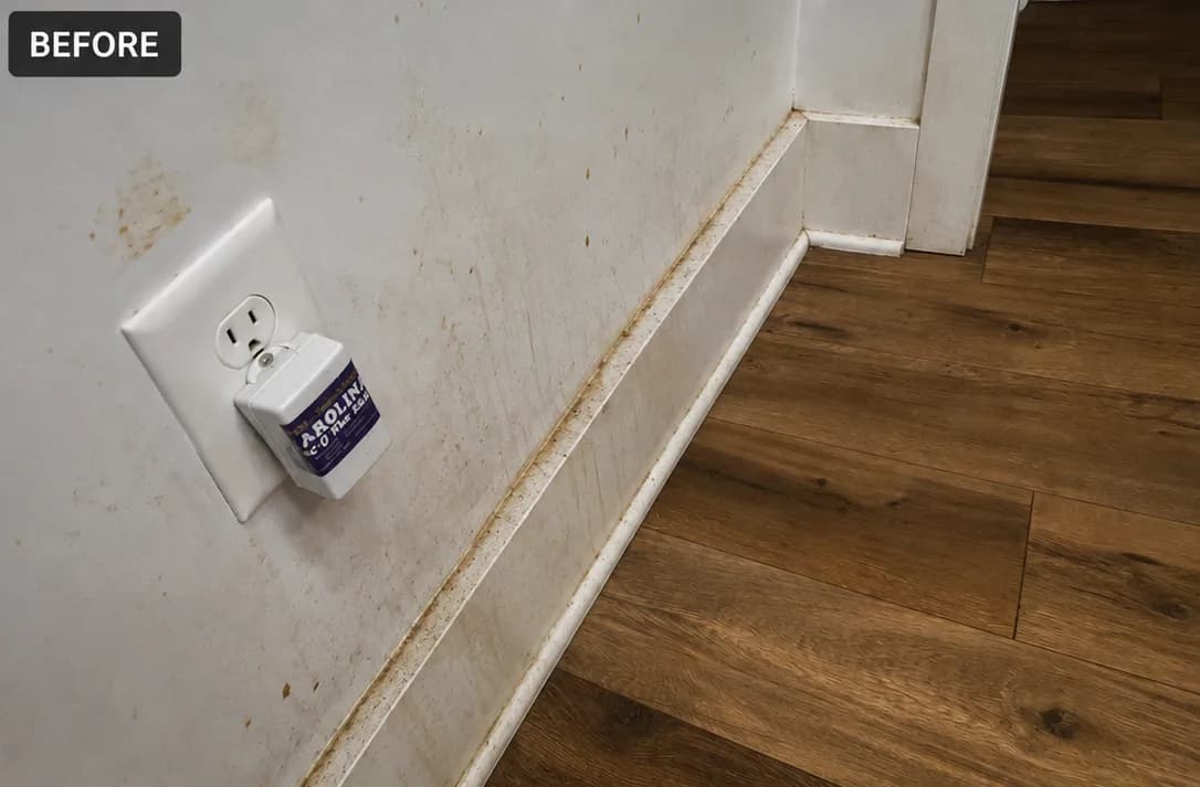 Electrical outlet on a dirty wall with water stains and damaged flooring before cleaning.
